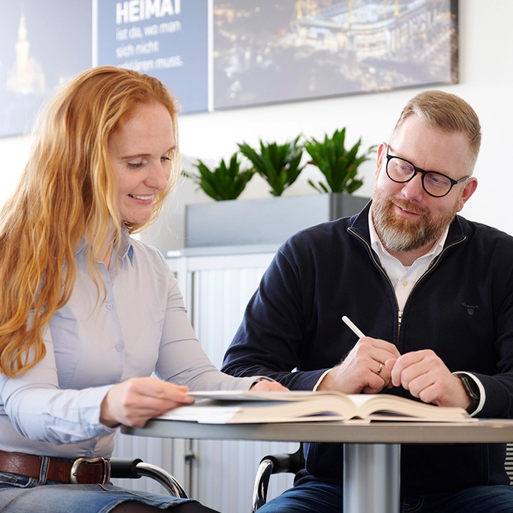 Un homme et une femme sont assis à une table et parlent d’un catalogue