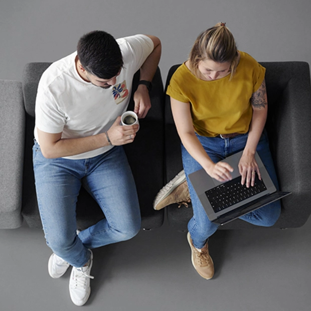 Ein Mann und eine Frau sitzen auf einem Sofa und schauen auf einen Laptop. 