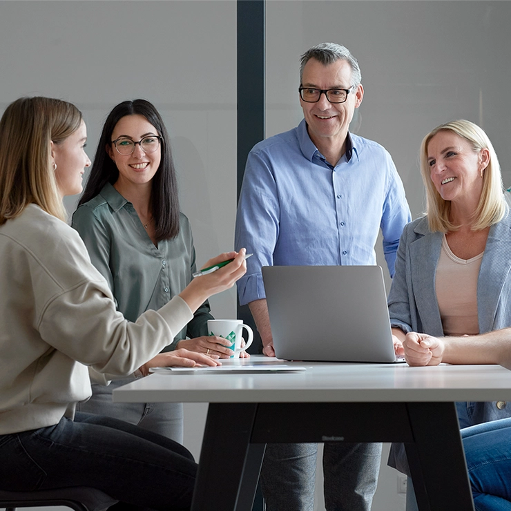 Three women and a man stand around a table laughing and chatting.