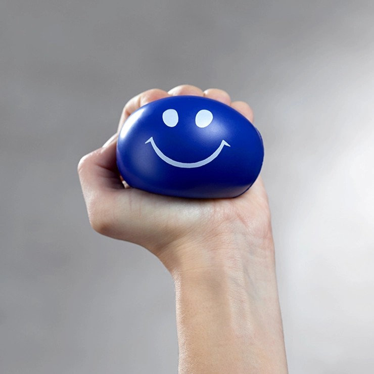 Hand mit einem blauen Stressball, der ein lächelndes Gesicht hat