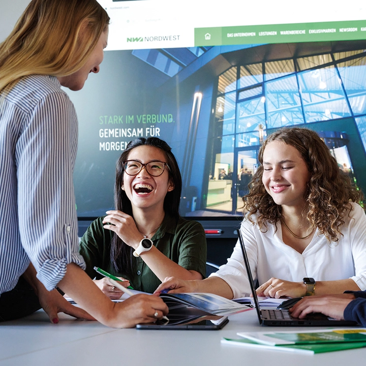 Drei junge Frauen lachen und arbeiten an einem Projekt